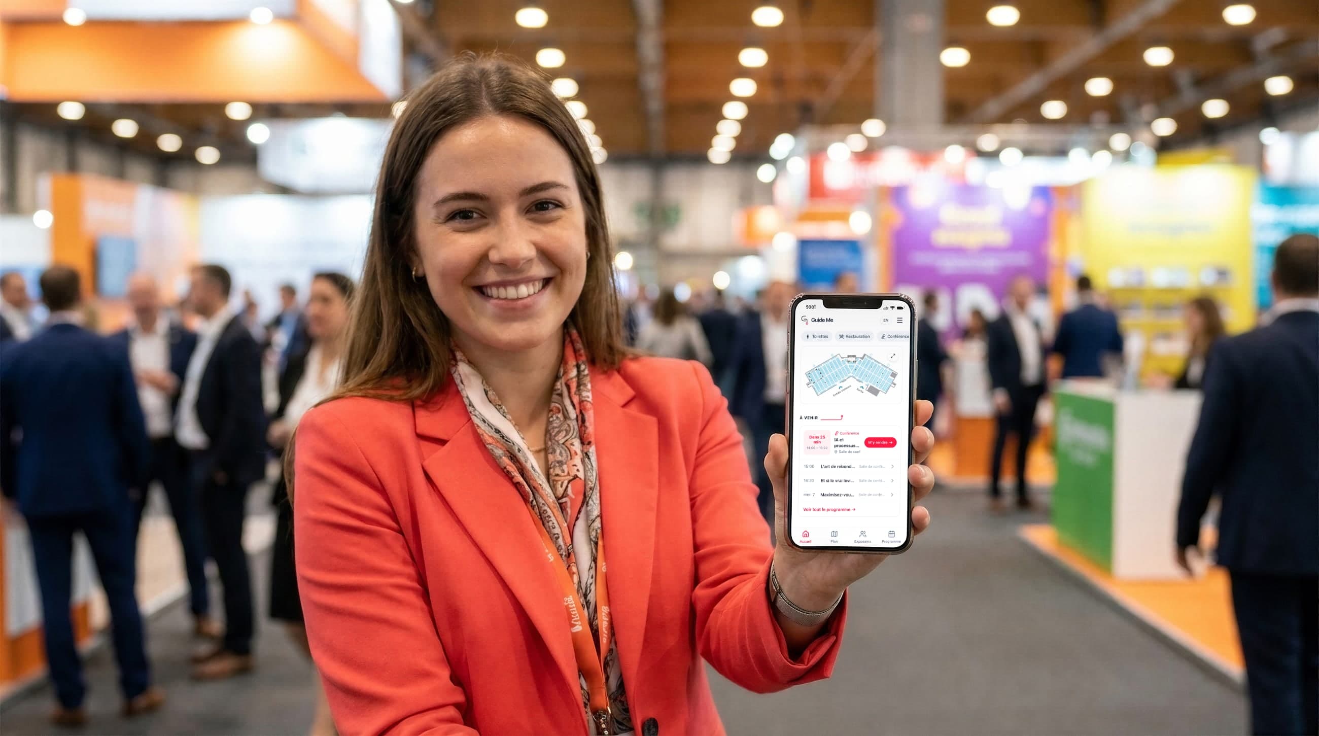 Une visiteuse souriante montre l’app du salon sur son téléphone : le plan de salle et le décompte avant la prochaine conférence